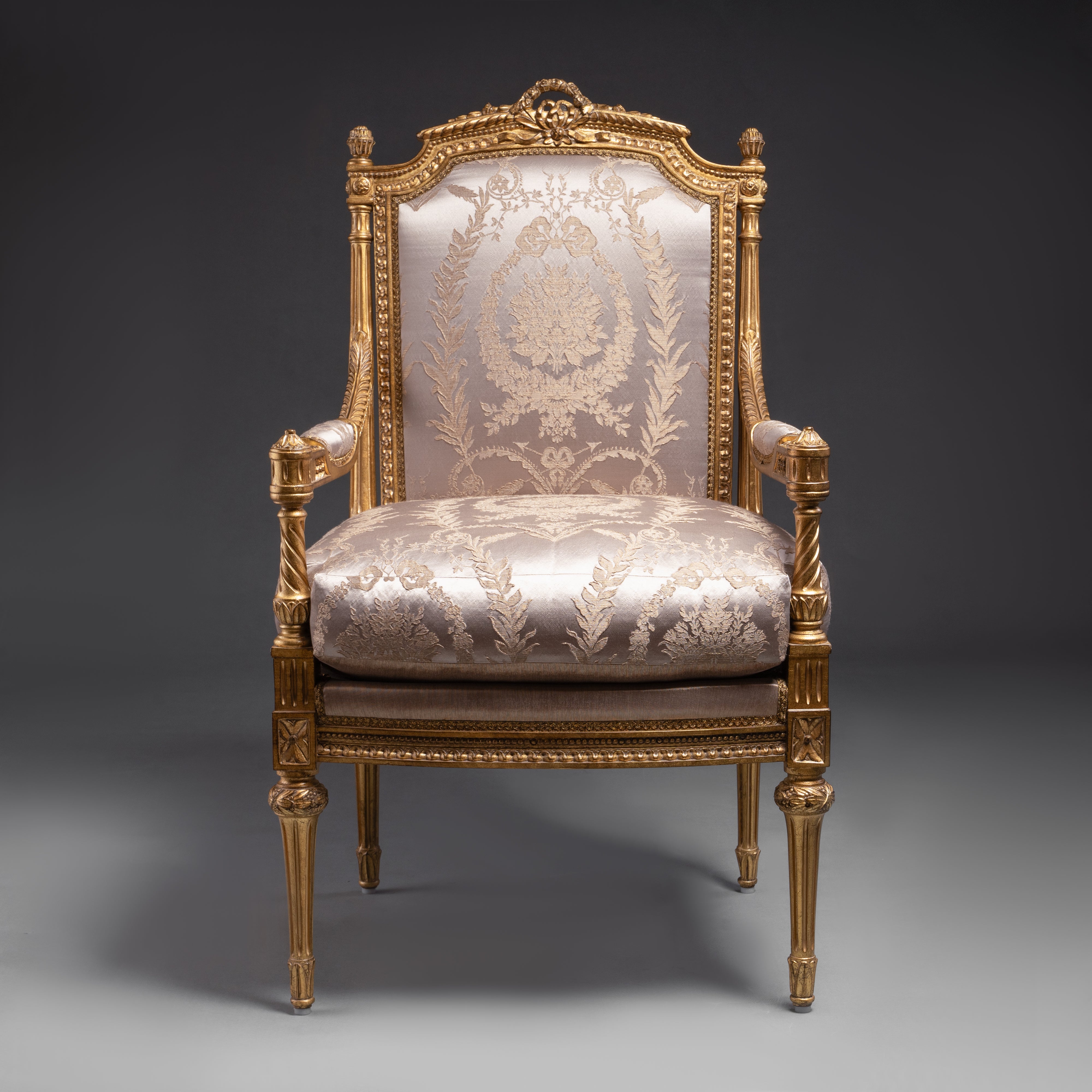 A luxurious Louis XVI-style armchair featuring  intricate gold leaf carvings and rich fabric  upholstery.