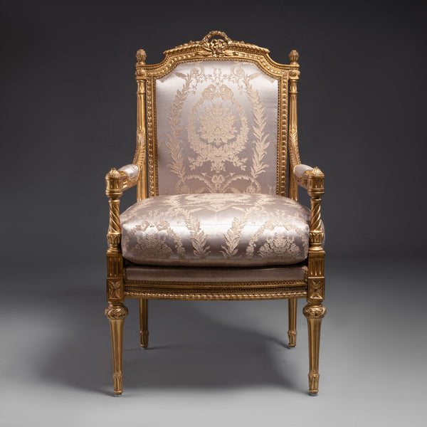 A luxurious Louis XVI-style armchair featuring  intricate gold leaf carvings and rich fabric  upholstery.