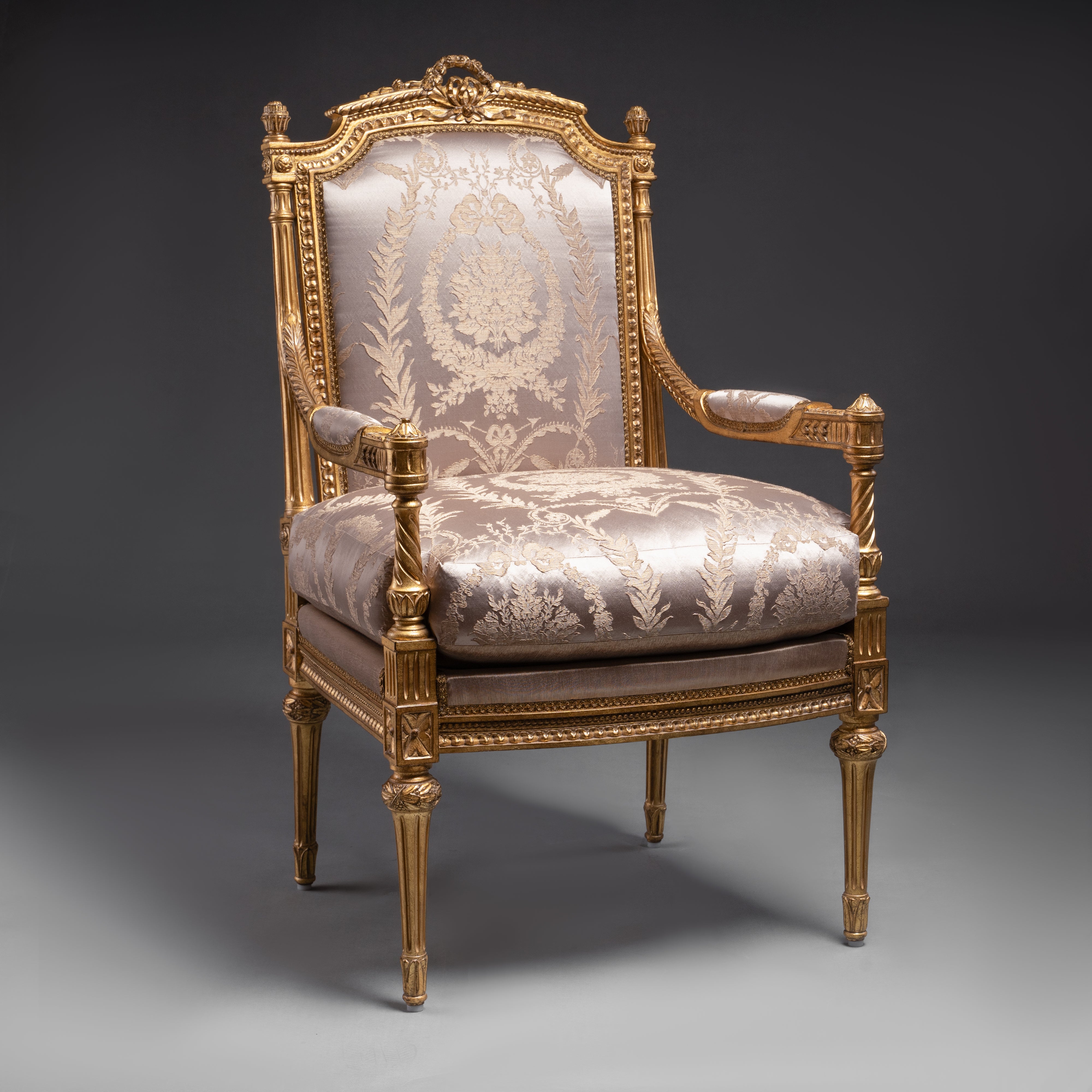 A luxurious Louis XVI-style armchair featuring  intricate gold leaf carvings and rich fabric  upholstery.