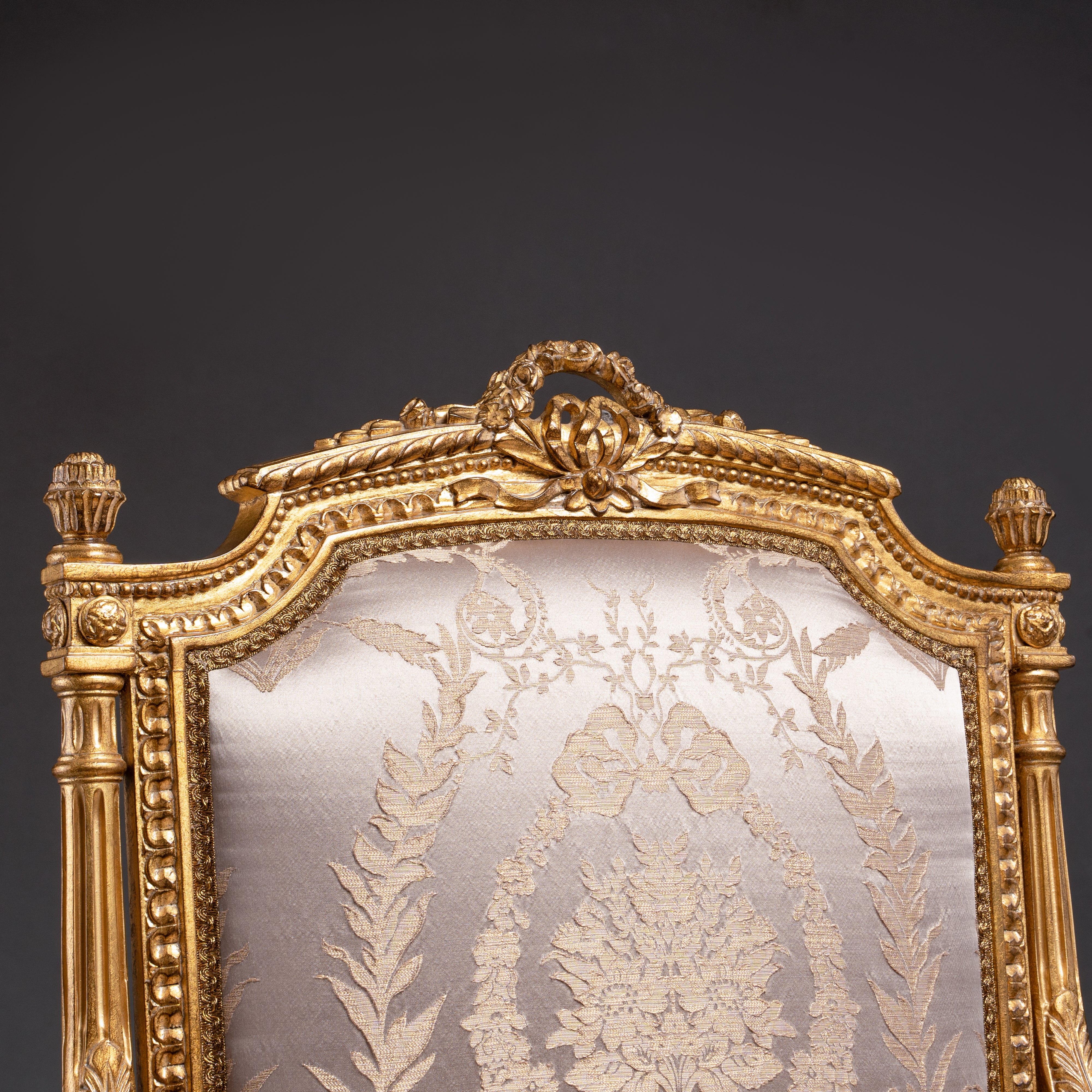 A luxurious Louis XVI-style armchair featuring  intricate gold leaf carvings and rich fabric  upholstery.