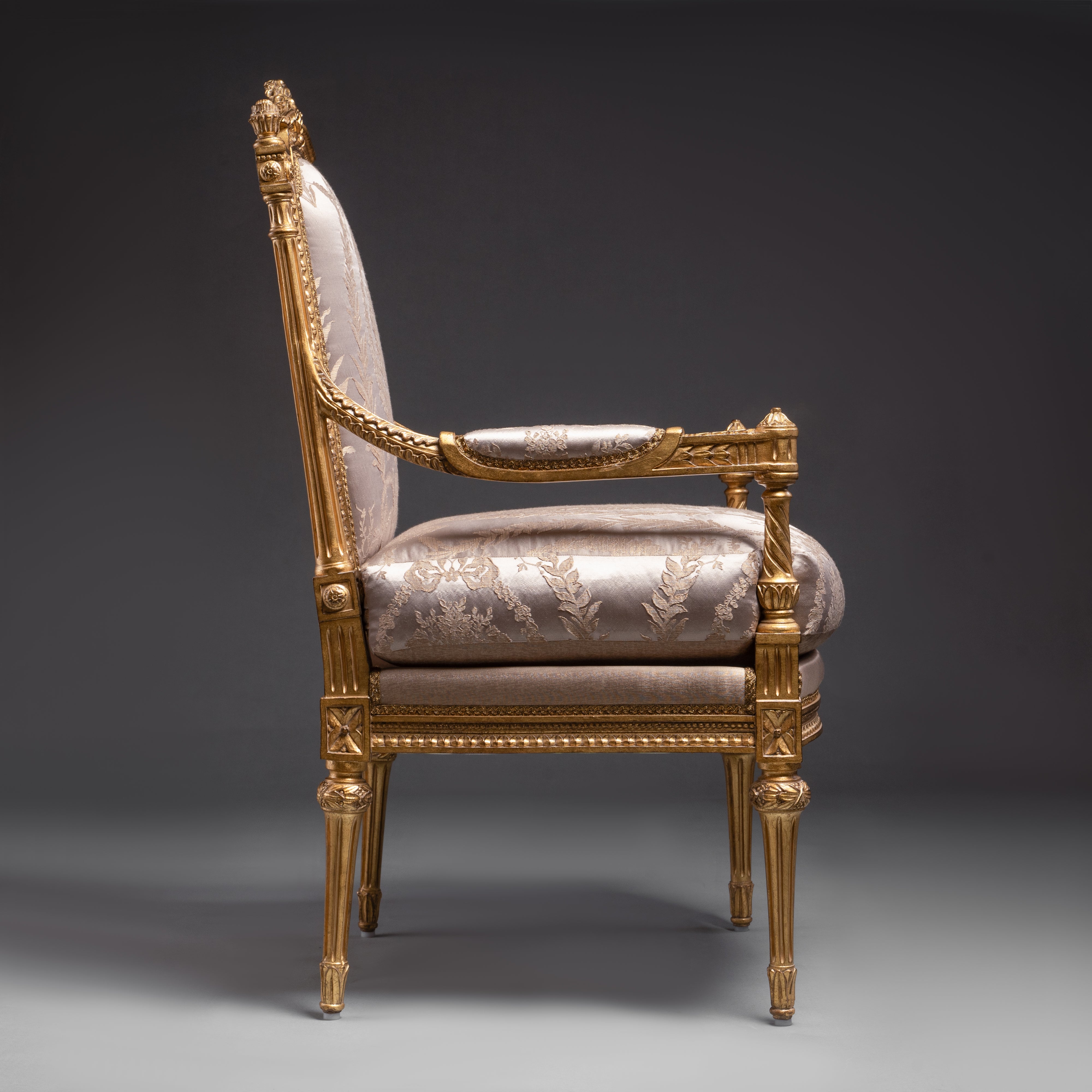 A luxurious Louis XVI-style armchair featuring  intricate gold leaf carvings and rich fabric  upholstery.