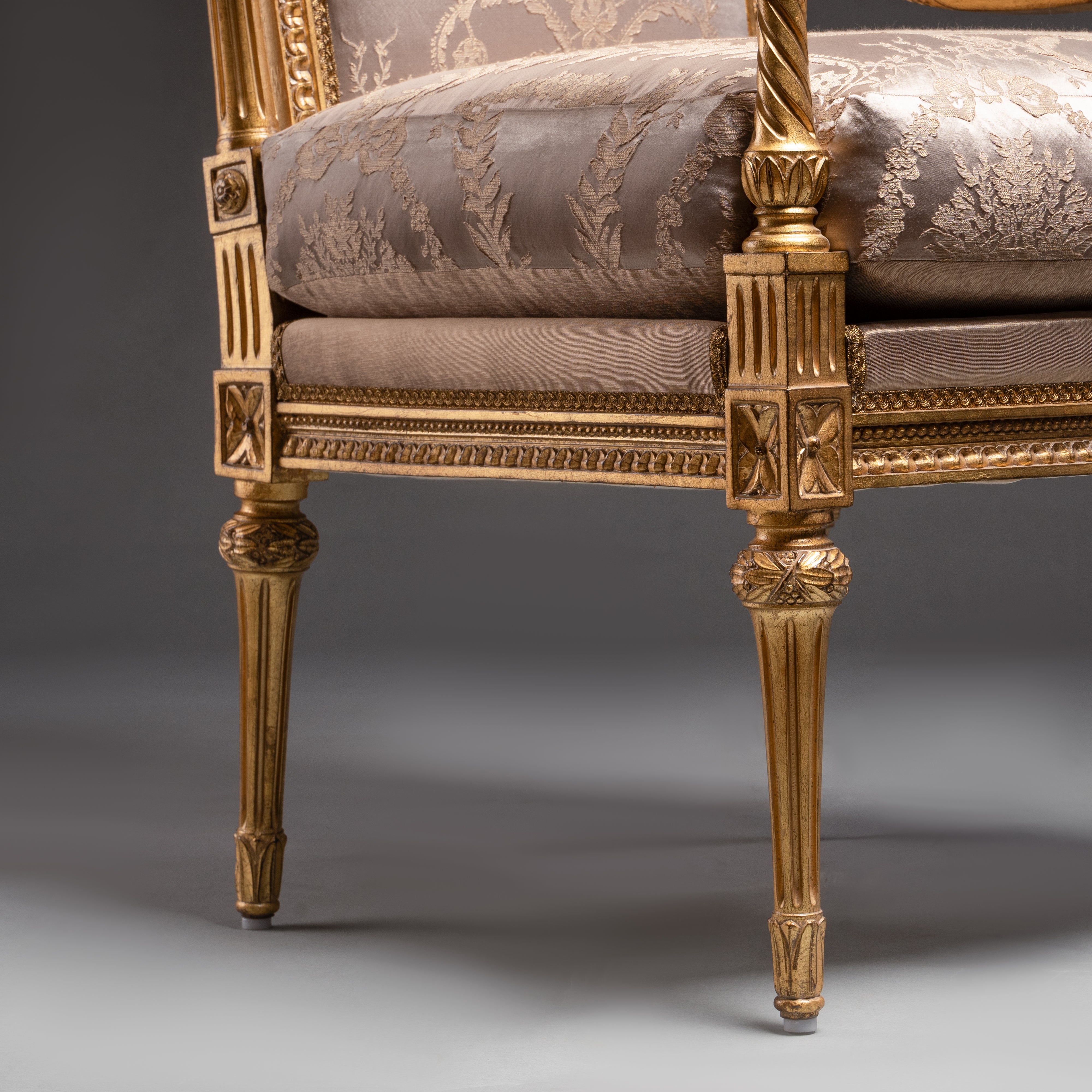 A luxurious Louis XVI-style armchair featuring  intricate gold leaf carvings and rich fabric  upholstery.
